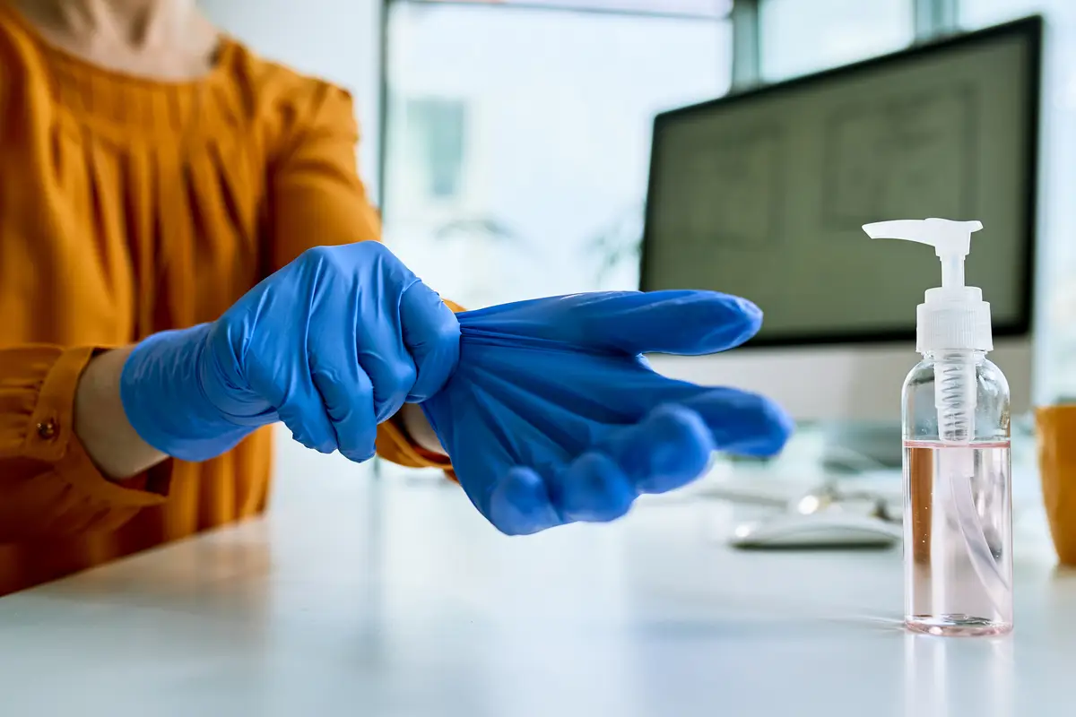A importância do cuidado com pele e unhas para profissionais de saúde 1 Closeup of businesswoman preparing for work and putting on protective gloves in the office
