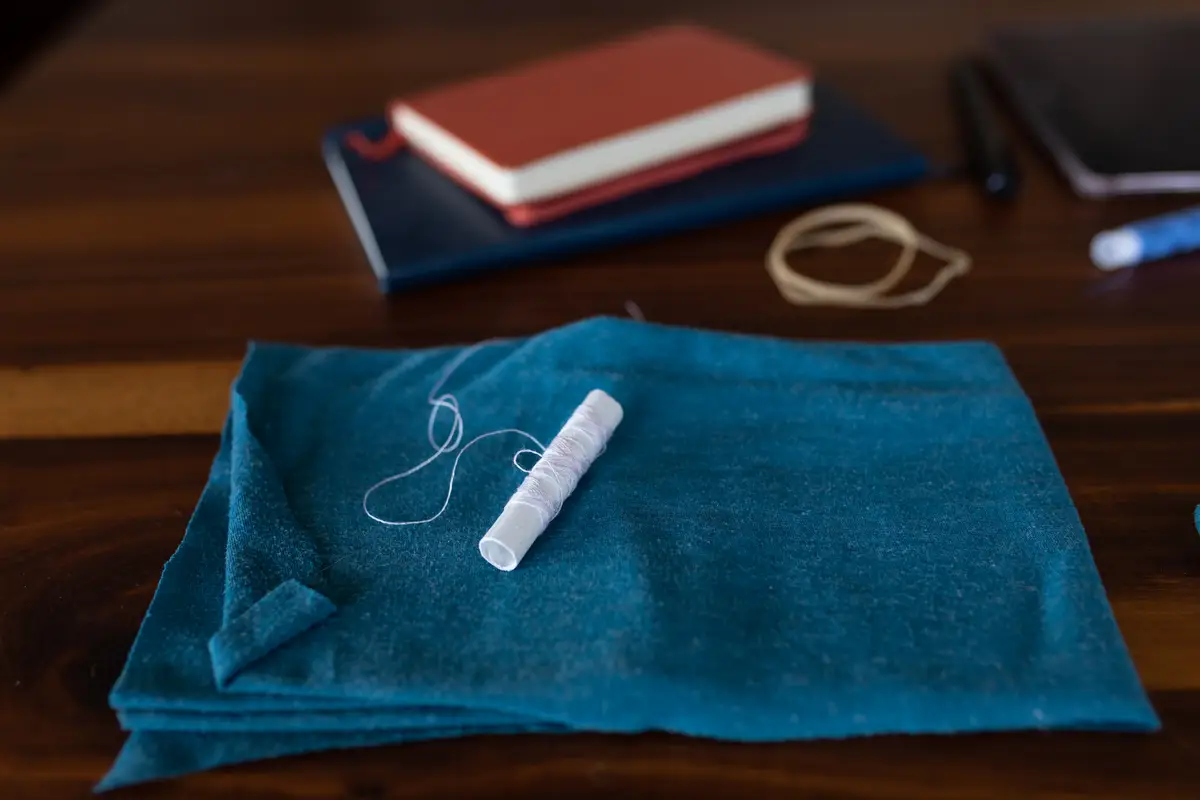 Close up of a piece of a blue material and a thread lying on a wooden table, used for making face masks against covid 19