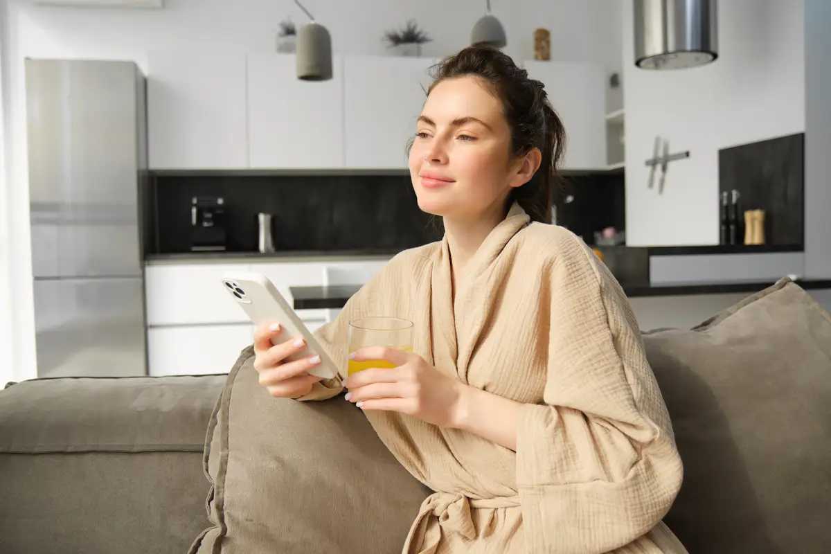 Beautiful young woman resting on sofa enjoying her morning at home holding glass of orange juice and