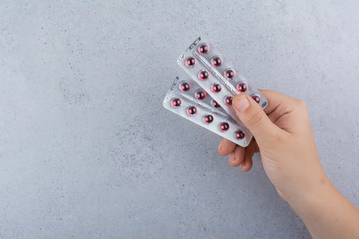 Woman hand holding two packs of pills on marble background.