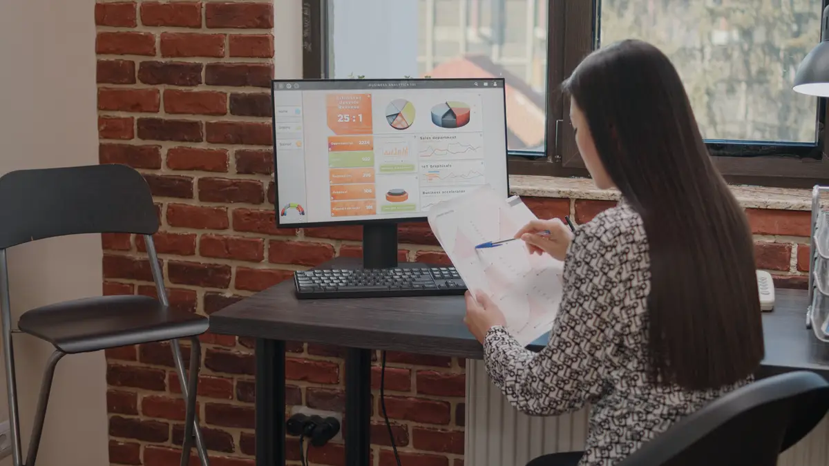 Close up of employee working with charts on papers and computer, doing annual data analysis to plan business project. Woman holding files with financial information for development.