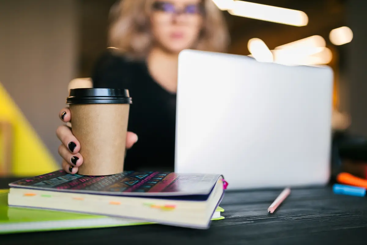 Hands of young pretty woman sitting at table in black shirt working on laptop in co-working office
