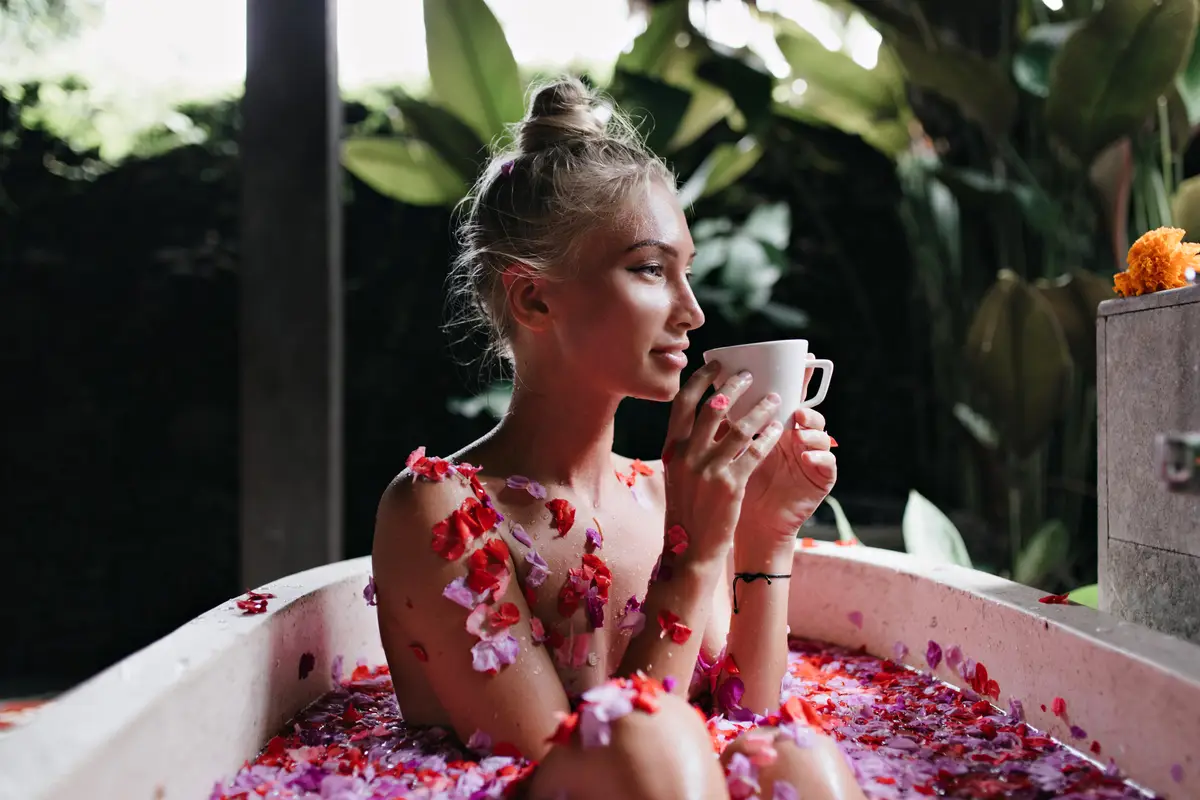 Pleasant woman sitting in bath on nature background and smiling. Adorable blonde woman drinking tea during spa in weekend.