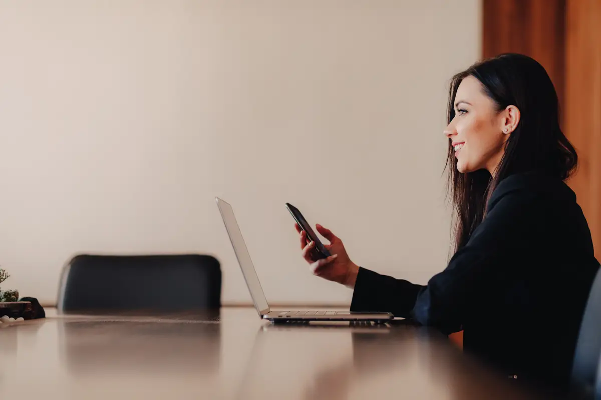 Young attractive emotional girl in business-style clothes sitting at a desk on a laptop and phone in the office or auditorium
