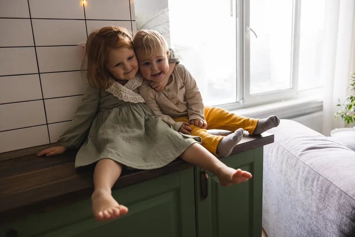 Friendly little caucasian brother and sister in casual clothes are fooling around with each other while sitting indoors during day Family concept