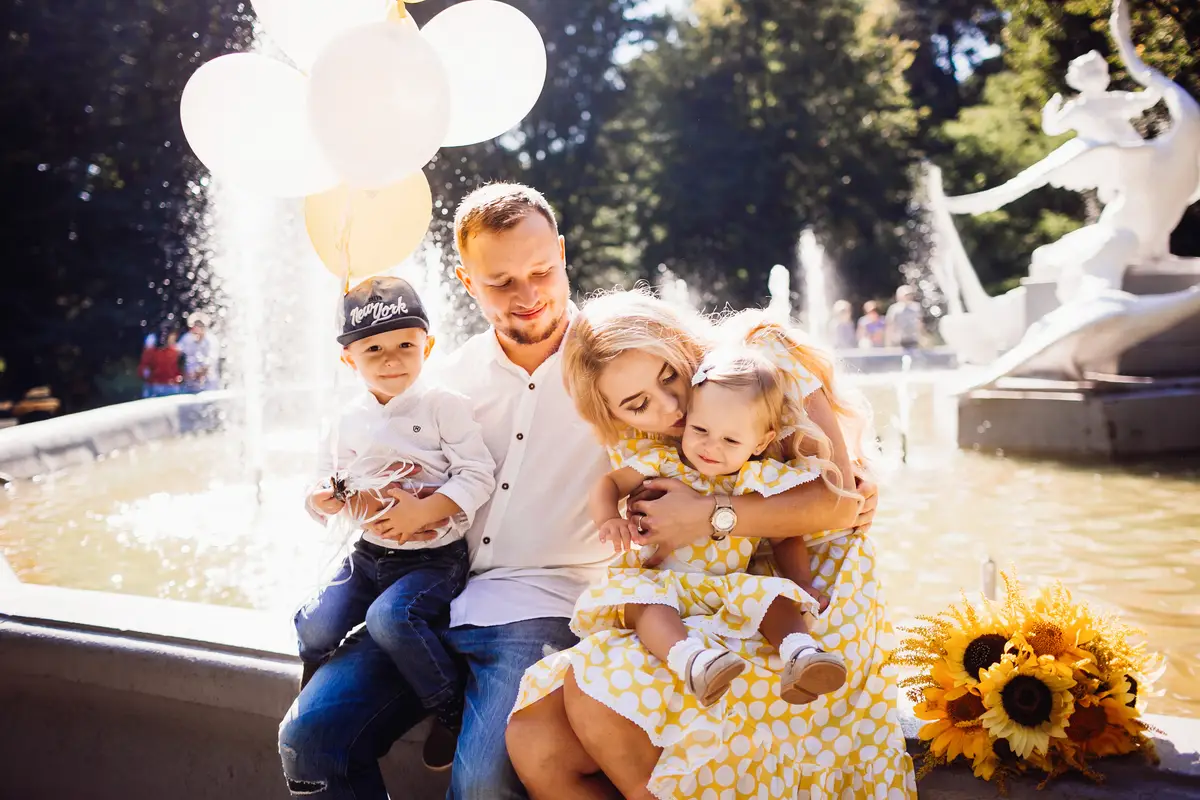 Lovely family dressed in the same clothes sits on the fountain with their children and yellow balloons