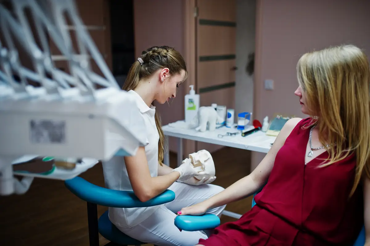 Gorgeous young orthodontist posing with big tooth model next to her pretty patient