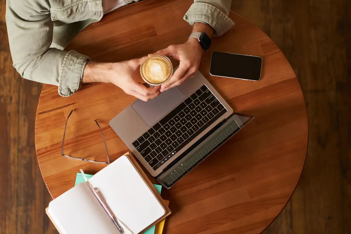 Top view male hands holding cup of coffee man sitting at round table in a cafe working on laptop had
