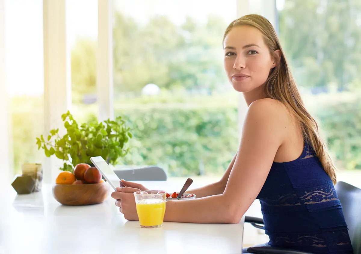 Woman breakfast and morning portrait with tablet strawberry bowl and orange juice for healthy nutrition Kitchen counter communication and social media or networking browse online and read blog
