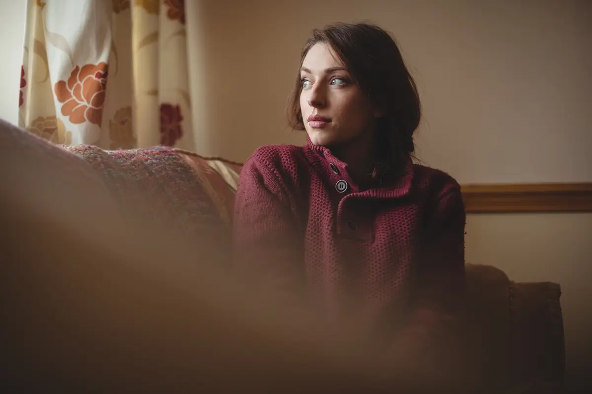 Thoughtful woman sitting on sofa in living room
