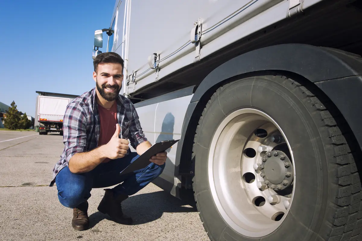 Truck driver with thumbs up inspecting tires condition and checking pressure