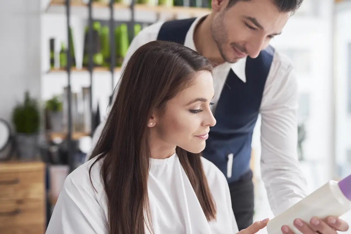 Hairdresser showing beauty product to female customer in salon