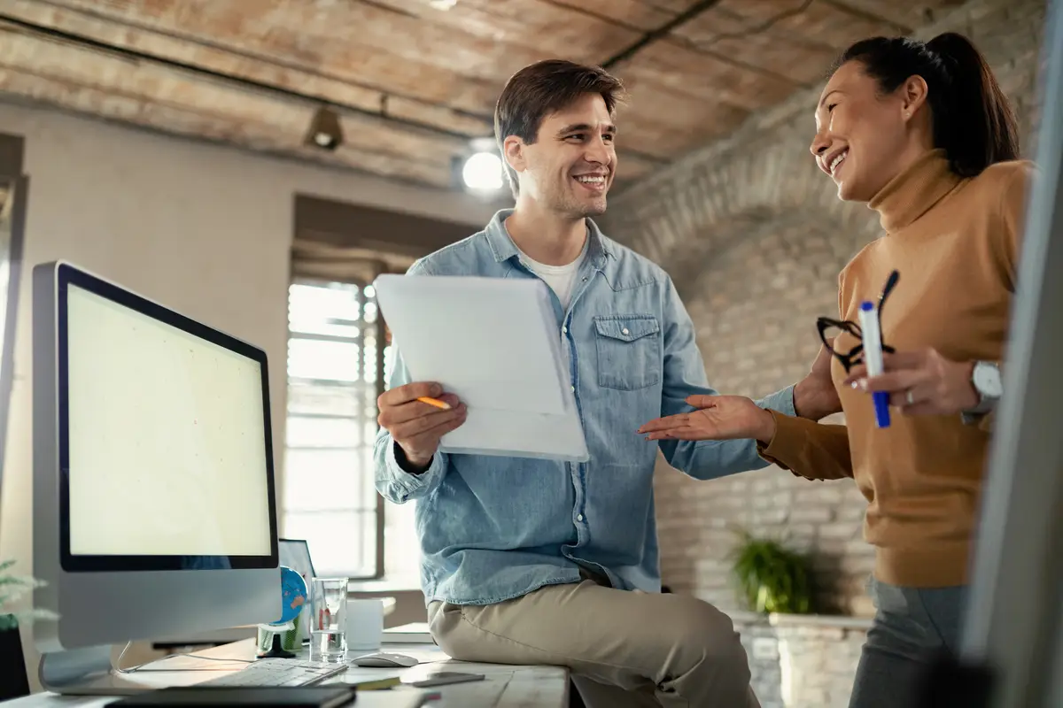 Two happy entrepreneurs analyzing business reports and communicating in the office