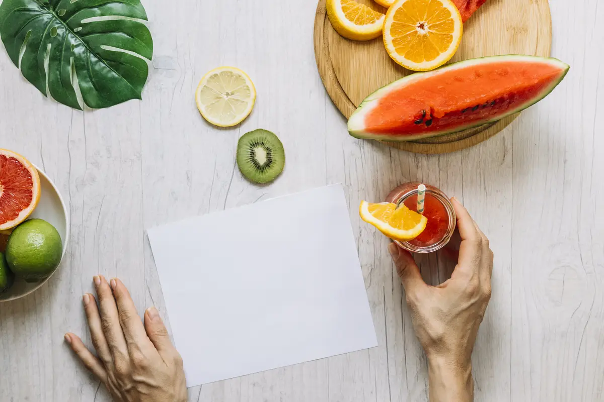 Crop hands with smoothie near fruits and paper sheet