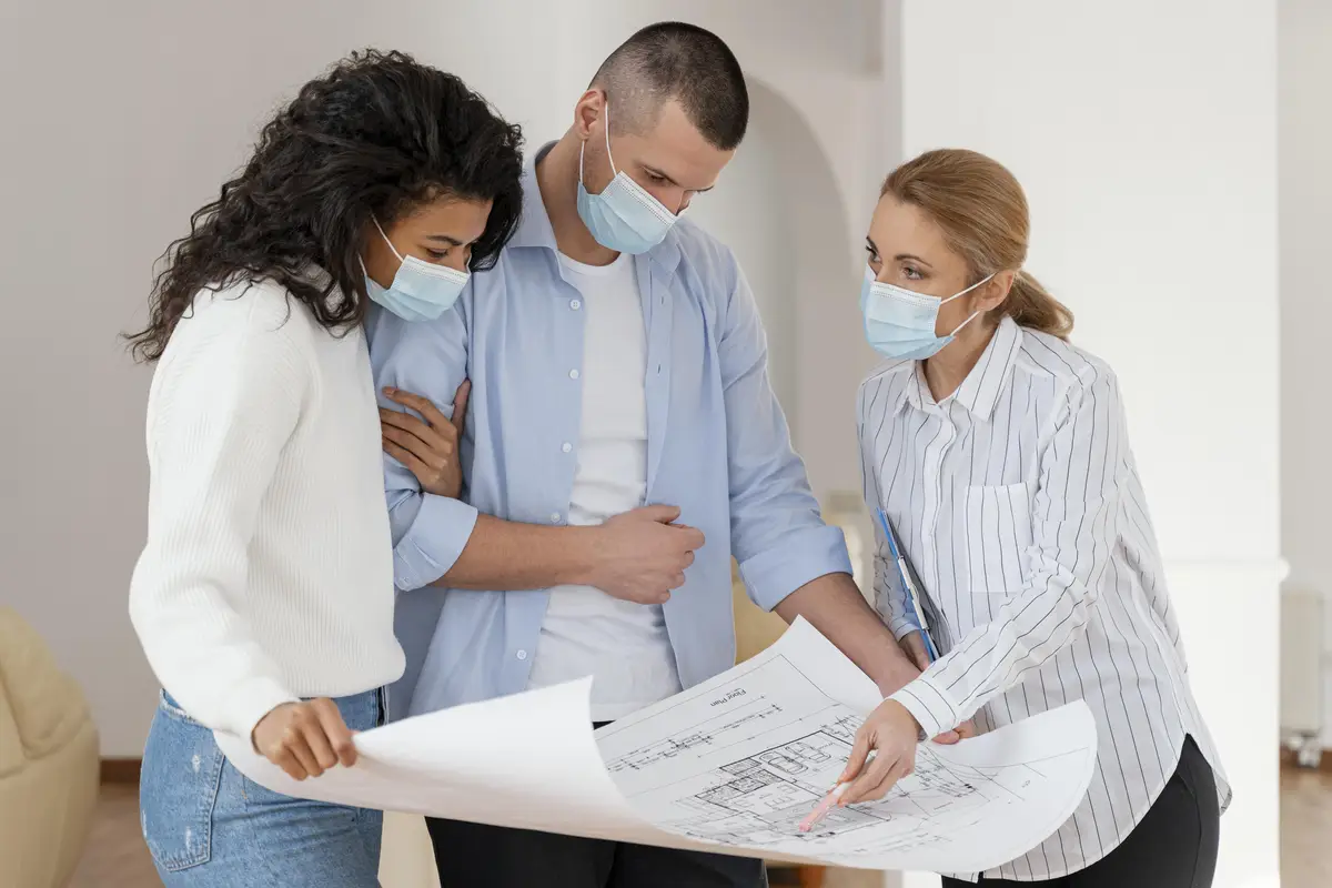 Realtor and couple with medical masks looking at house plans