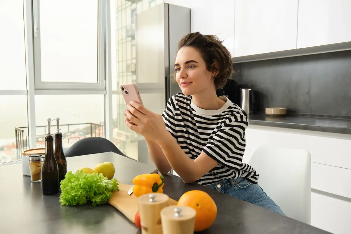 Portrait of brunette girl cooking food in the kitchen searching recipes on social media app holding