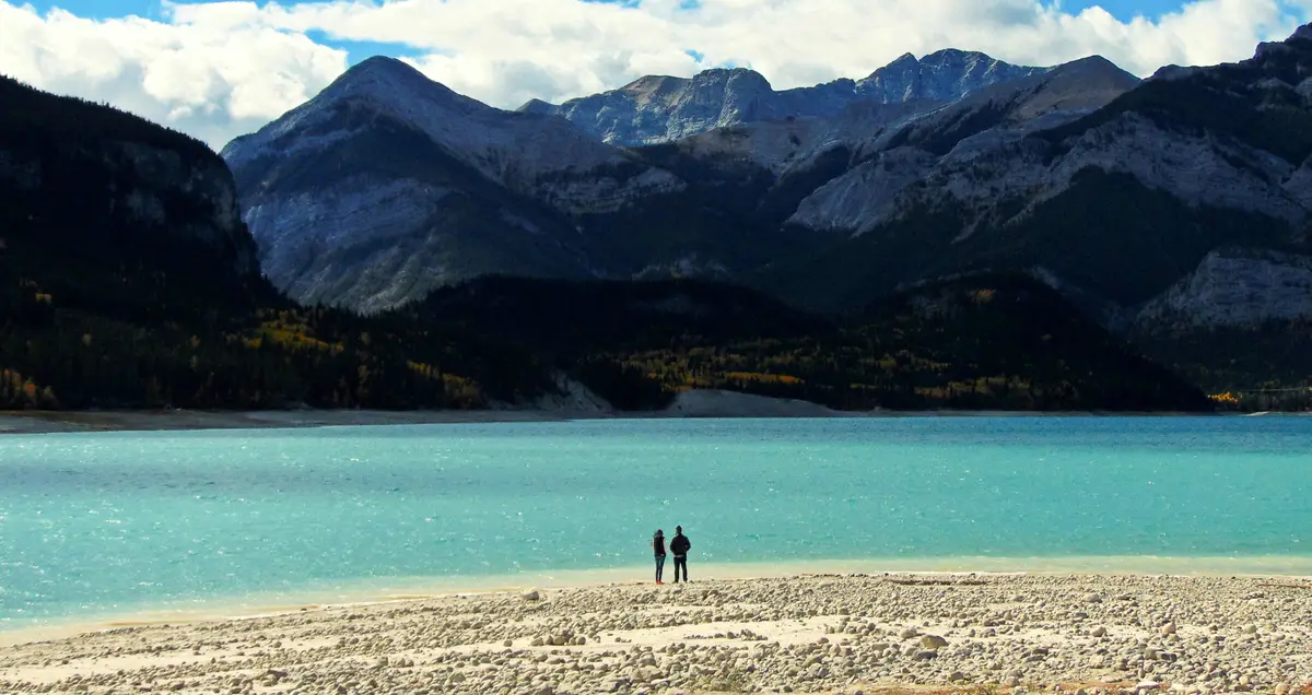 Friends standing on lakeshore against mountain