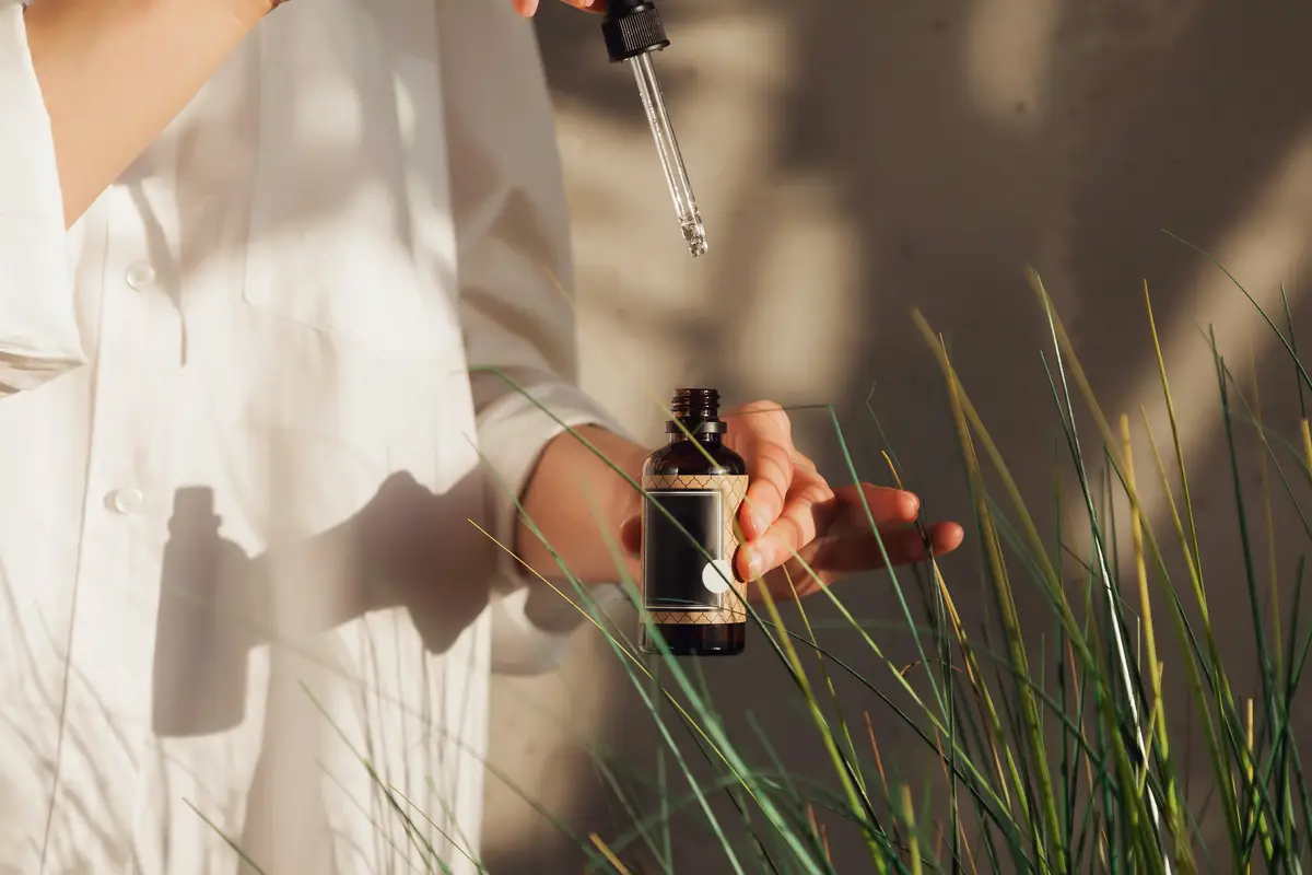 Woman hands holding massage or cosmetics oil bottles. Close up essential oil on chair. High angle view of massage oil bottle on leaf background. Concept of healthy lifestyle and self care. Copy space