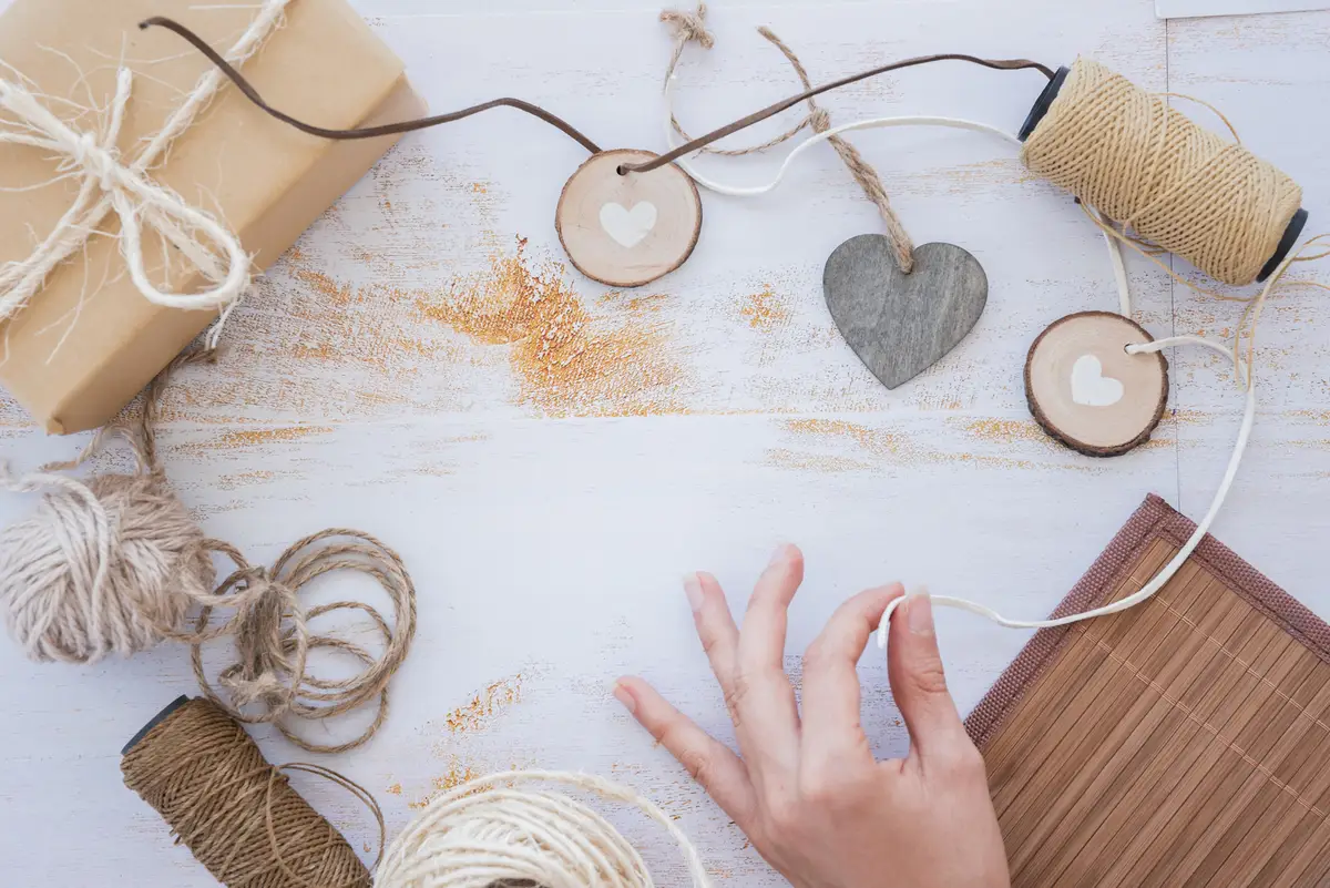 Close-up of hand making heart garland with spool and wrapped gift box on white desk