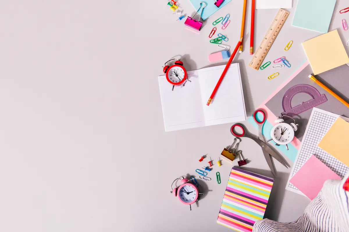Desk covered with school supplies and colorful alarm clocks.