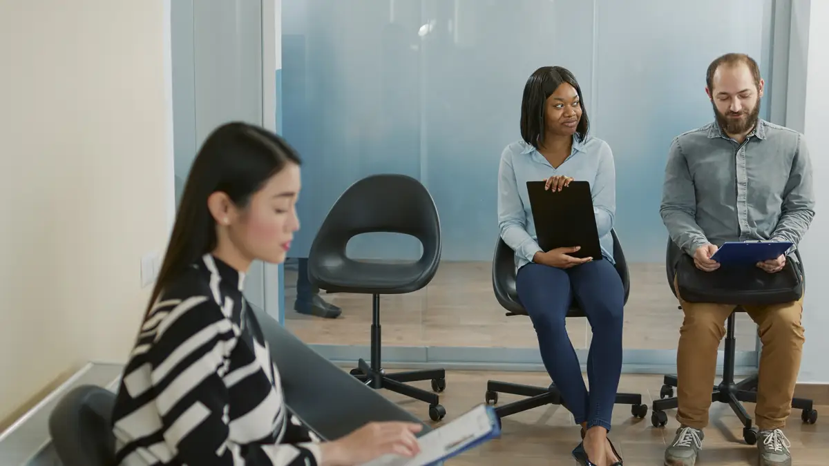Diverse group of candidates having conversation in office lobby, waiting to attend job intervew appointment. Man and woman talking about career opportunity and application with cv resume.