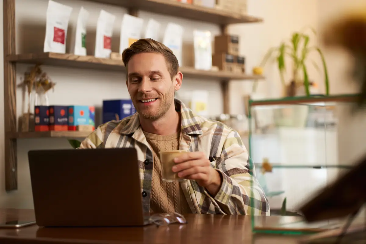 Lifestyle portrait of young businessman freelancer sitting in cafe drinking coffee and using laptop