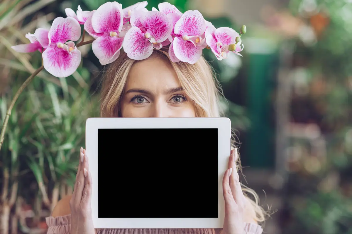 Pink orchid branch over her head holding blank digital tablet in front of her mouth