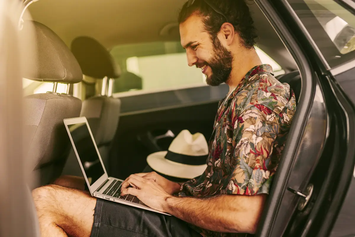 Cheerful blogger using laptop in car