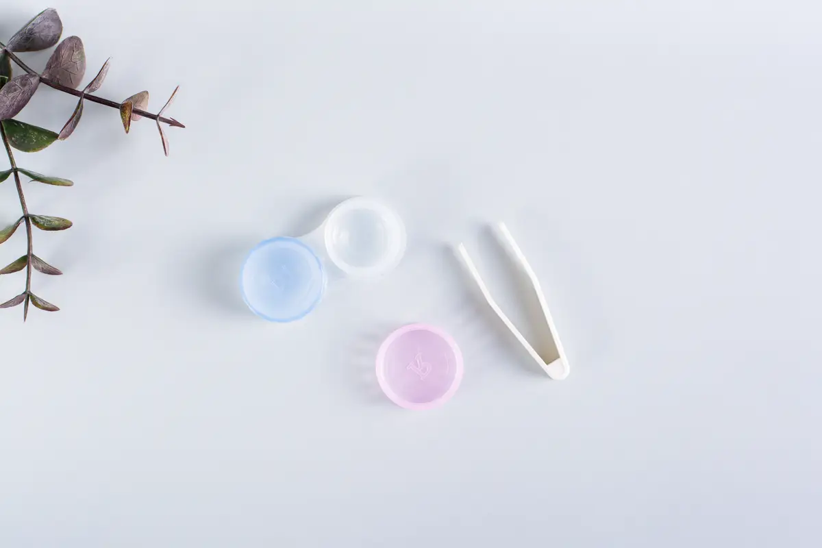An open container with contact lenses and tweezers on a blue background Top view