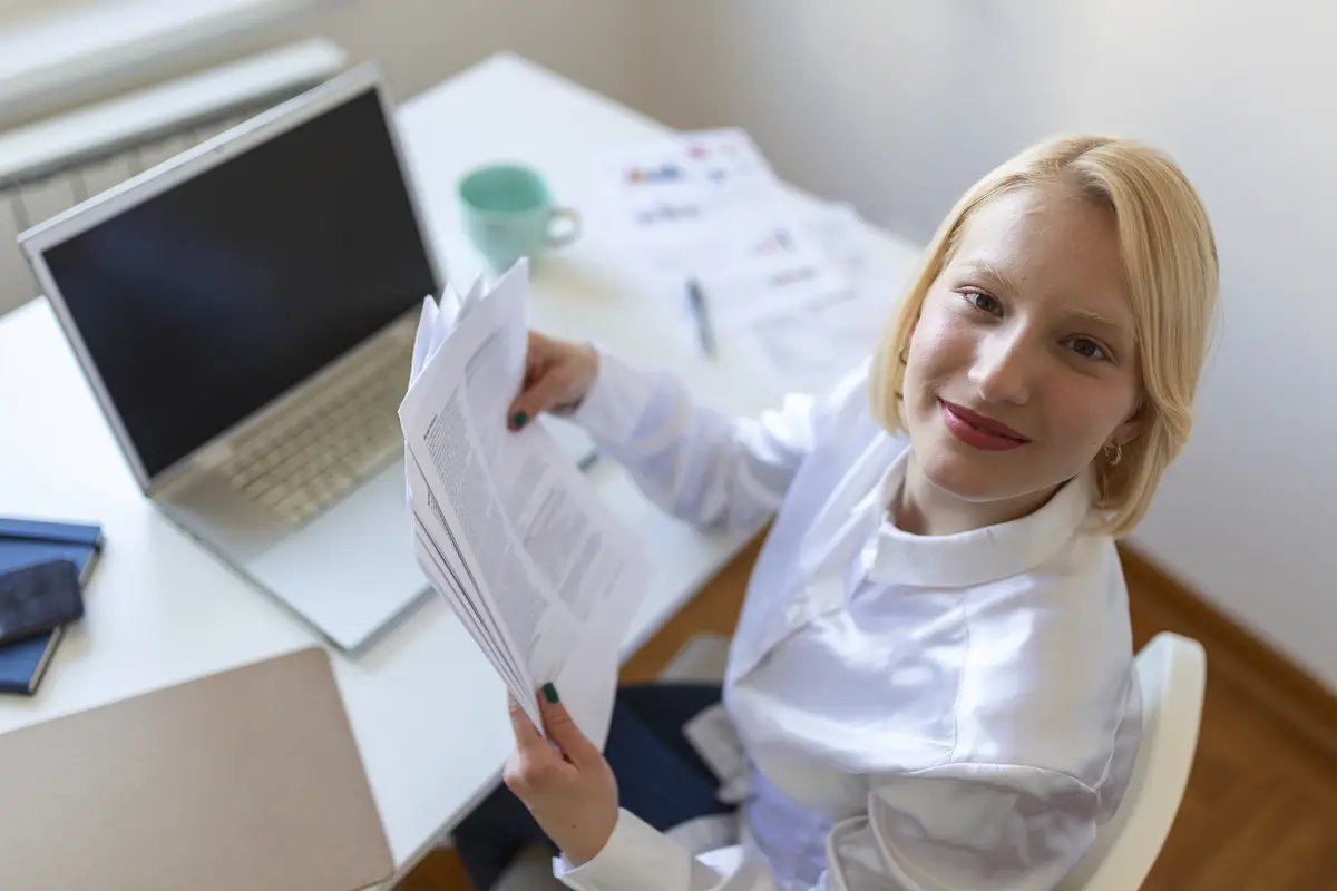 Remote job technology and people concept happy smiling young business woman with laptop computer and papers working at home office during the Covid19 health crisis