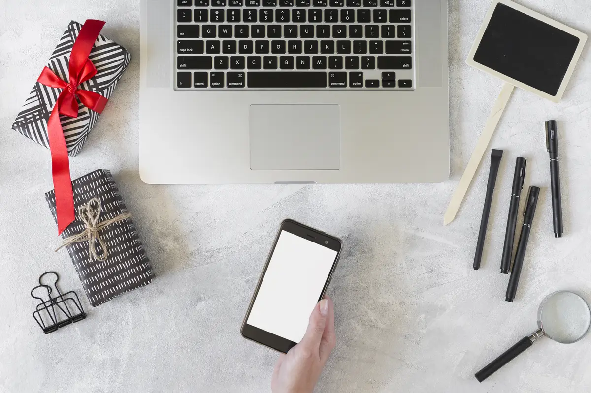 Hand with smartphone near laptop, present boxes and stationery