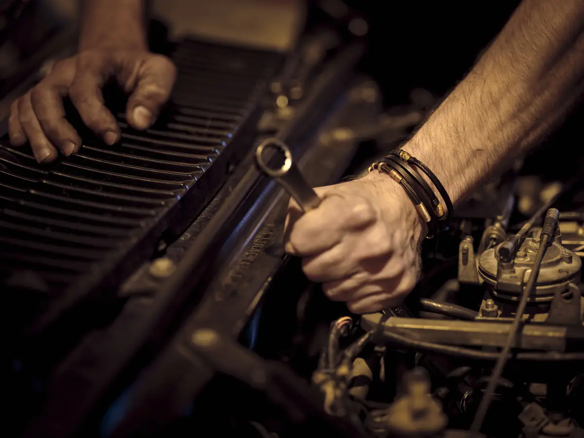 View of a man's strong hands with leather bracelets fixing the gear of a machine