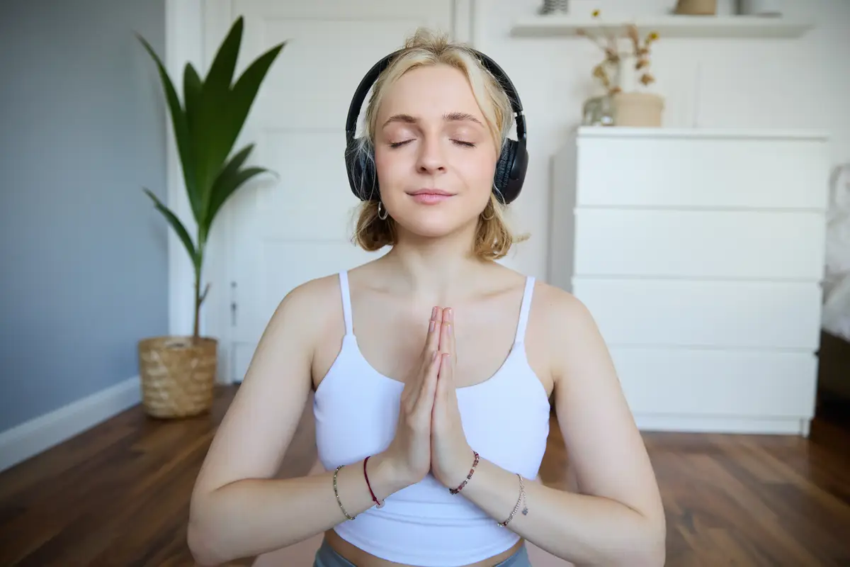 Portrait of woman meditating at home sitting in headphones listening to yoga podcast holding hands