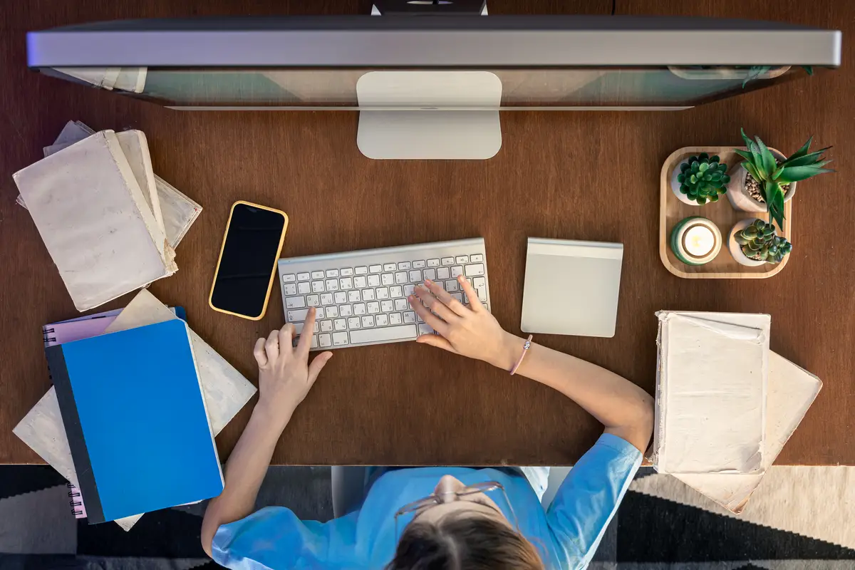 A schoolgirl with a smartphone sits in front of a computer studying online