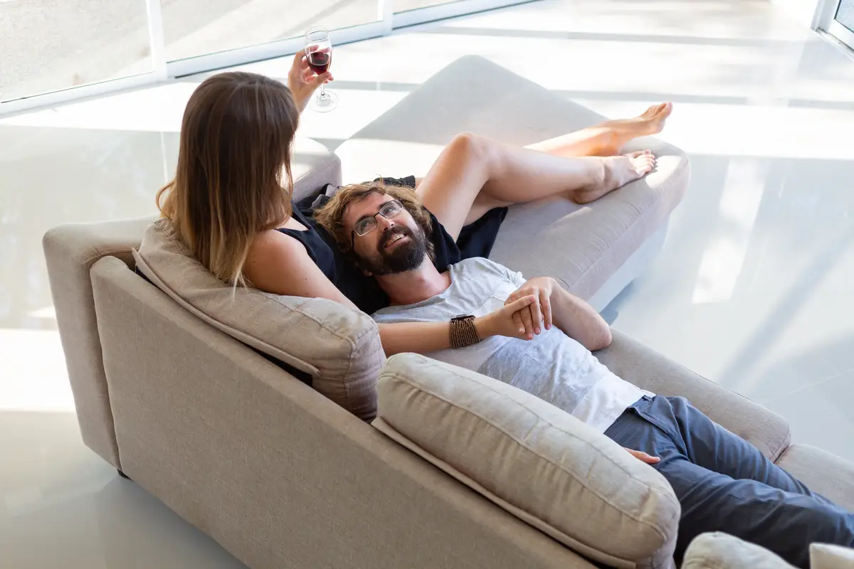 Happy couple relaxing, drinking wine and talking while sitting on couch. Romantic moments at home.