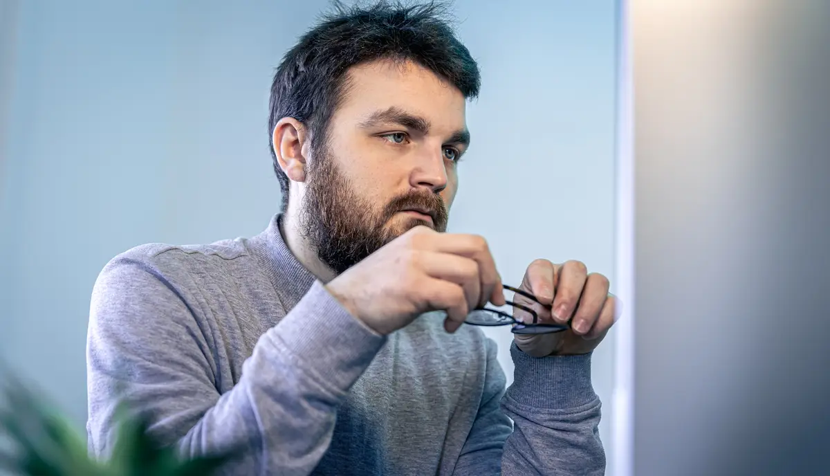 A man with glasses and a beard in front of a computer screen