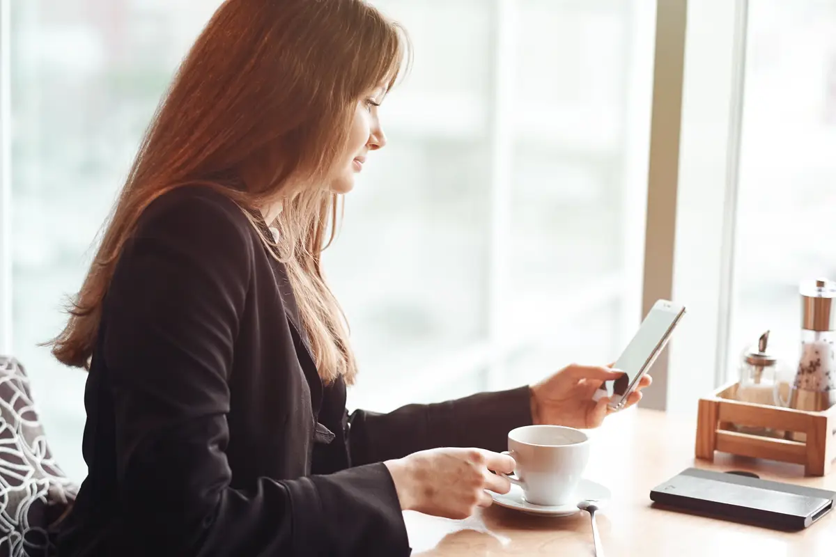 Young business woman using her smart phone and smiling in coffee shop