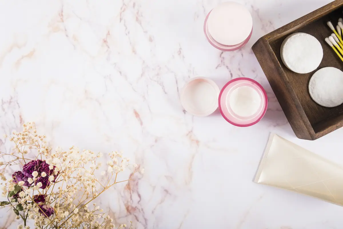 Overhead view of moisturizing cream and flowers on marble
