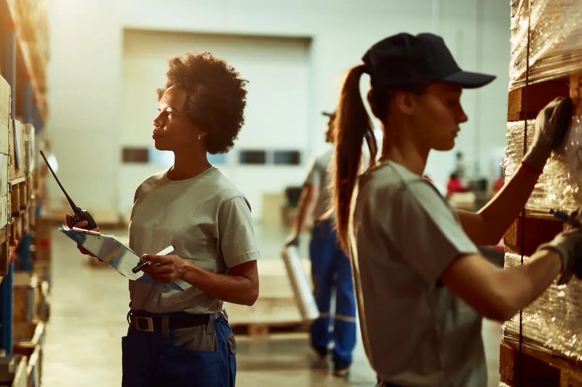 Black female inspector with walkietalkie checking stock of products while working in a warehouse