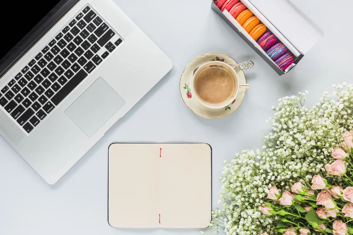 Laptop; coffee cup; macaroons and flowers bunch on white background