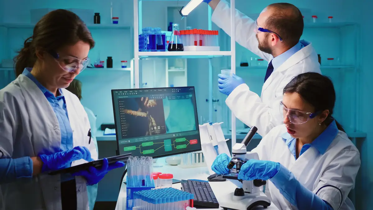 Manejo atual de meningite 2 Team of positive scientists working in chemistry equipped laboratory, nurse typing on tablet