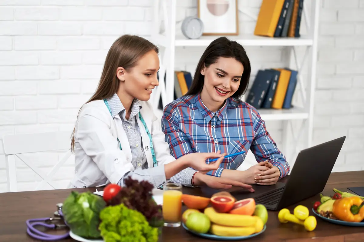 A smiling nutritionist advises a young patient woman on proper nutrition and dieting