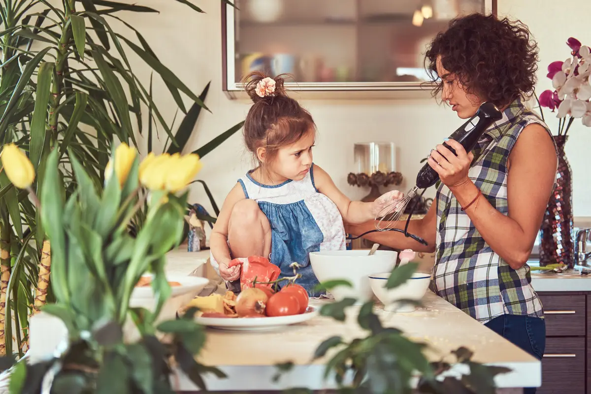 Beautiful curly Hispanic mother teaches her cute little daughter prepare pizza in the kitchen.