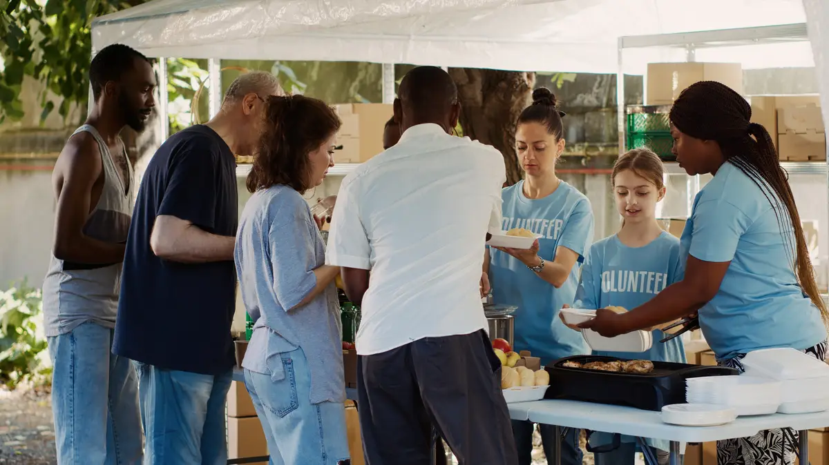Outdoor food distribution event organized by a non-profit, drawing people of all races who want to help the homeless and less fortunate. Warm meals are provided by volunteers to the poor and needy.