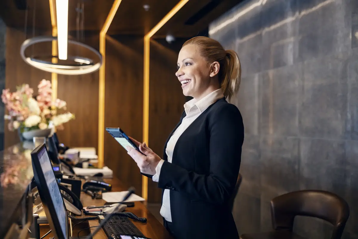A happy receptionist is talking with hotel guest and making a reservation on a tablet