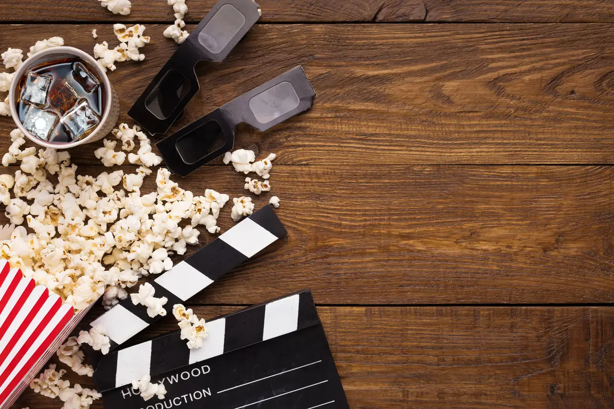Cinema background, top view. Clapperboard, popcorn, soda and 3D glasses on wooden table, copy space. Movie goers accessories, cinematography concept