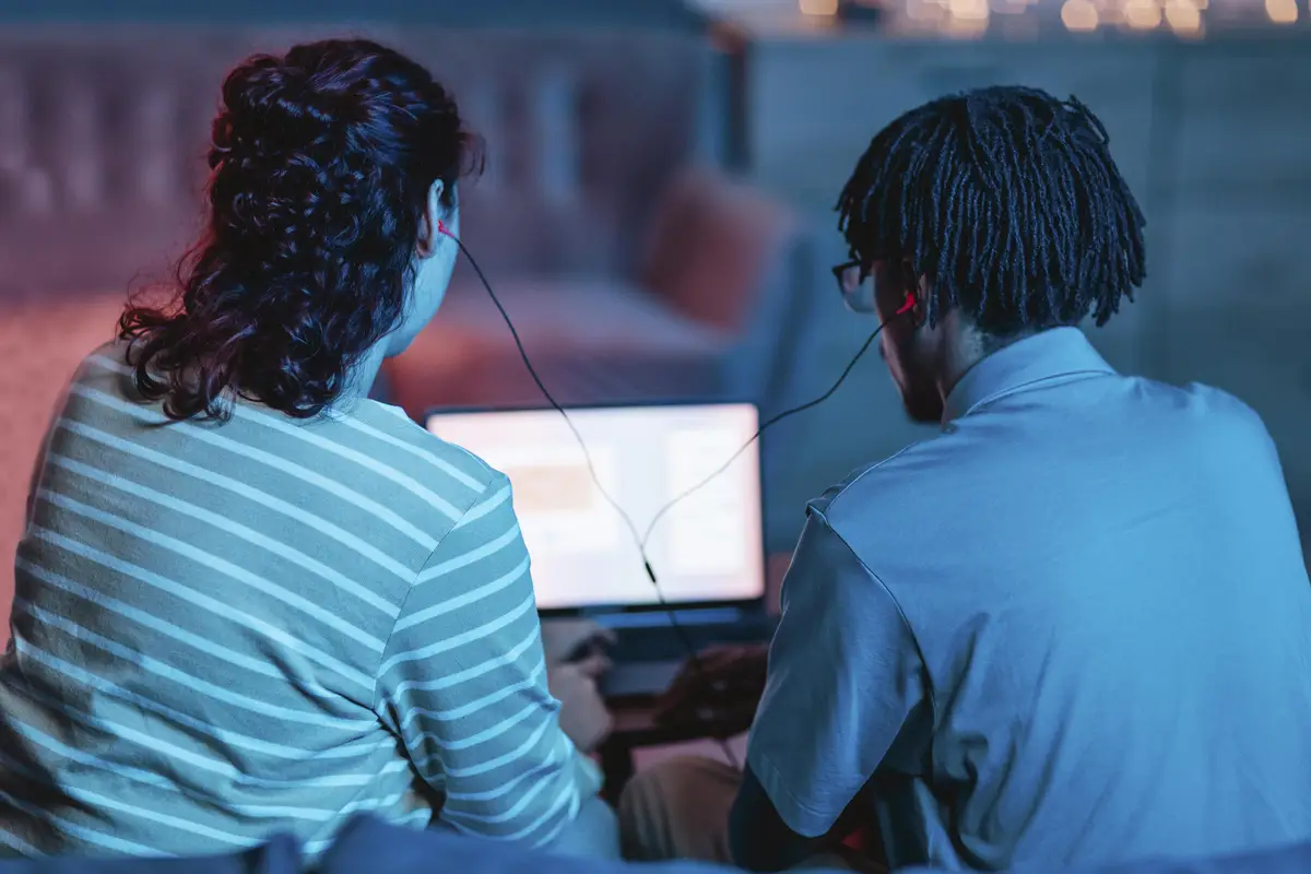 Back view of couple using laptop and earphones at home