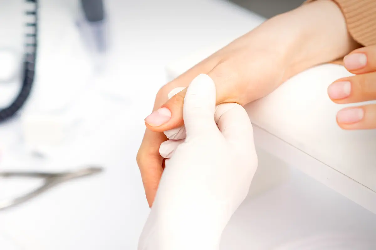 The manicurist holds the female thumb during a manicure procedure in the nail salon.