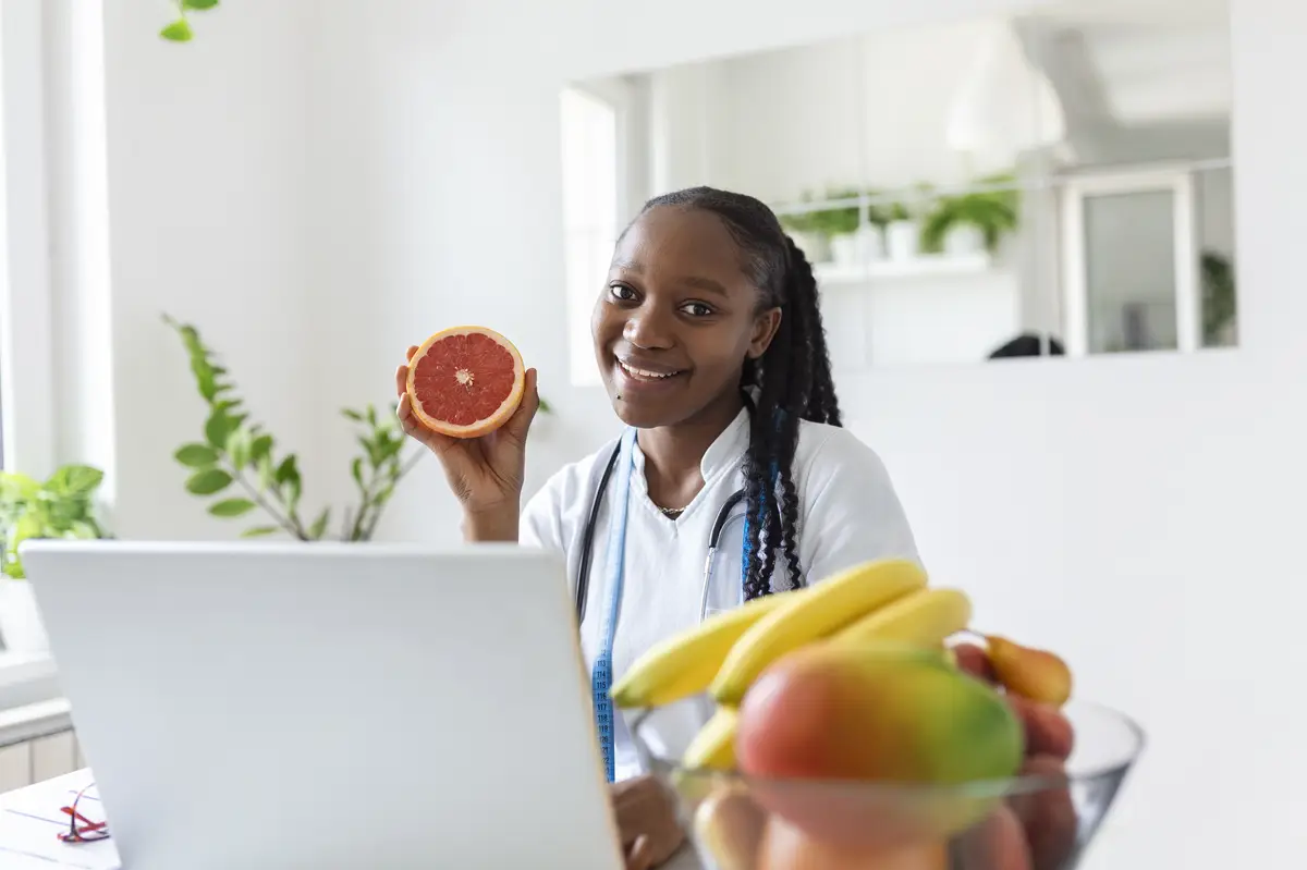 Portrait of young smiling female nutritionist in the consultation room Nutritionist desk with healthy fruit juice and measuring tape Dietitian working on diet plan