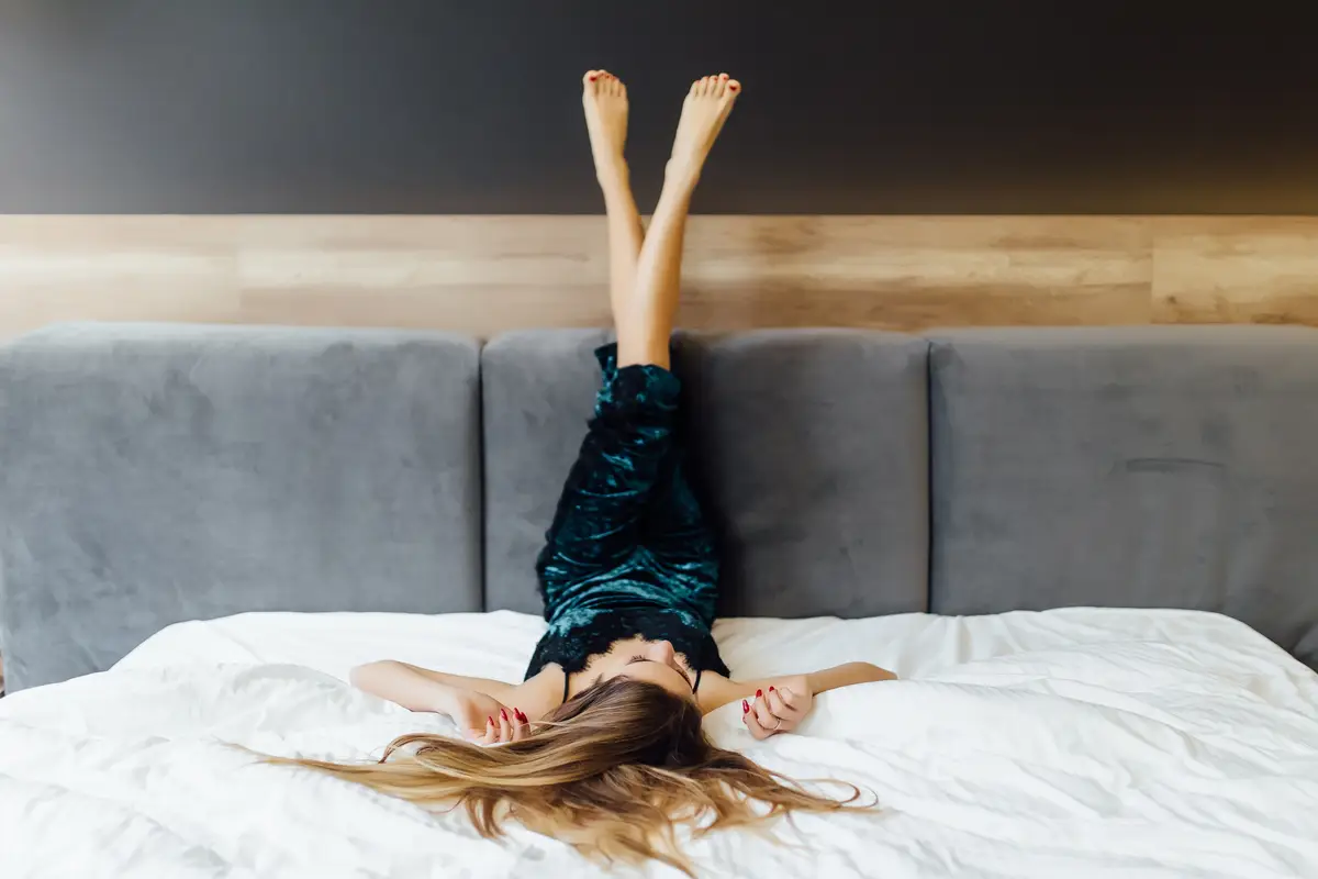 Young woman in blue pajamas posing on his bedroom, crossed legs